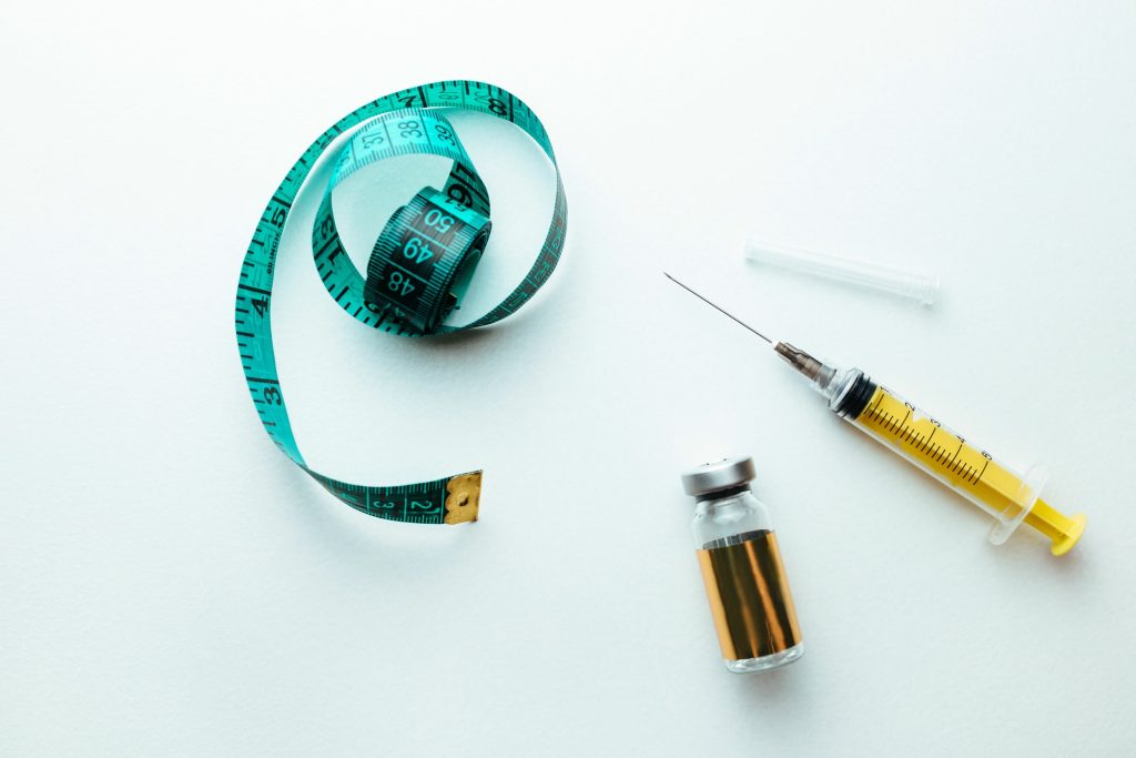 lipolytic and syringe on a white background next to a measuring tape for the body. The concept of losing weight and burning fat in a cosmetic way
